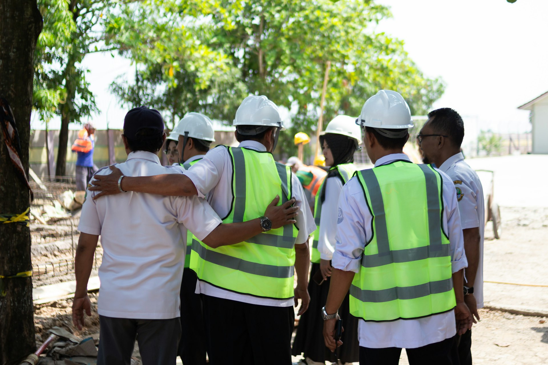 Construction workers in hard hats and vests huddle together.